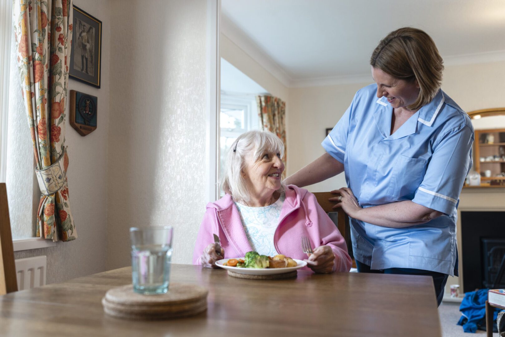 Caregiver assisting elderly woman during meal.