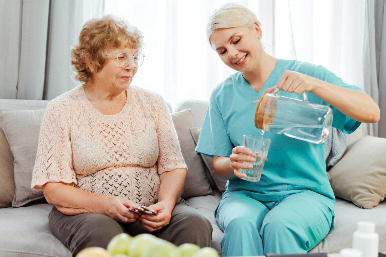 Caregiver pouring water for elderly woman.