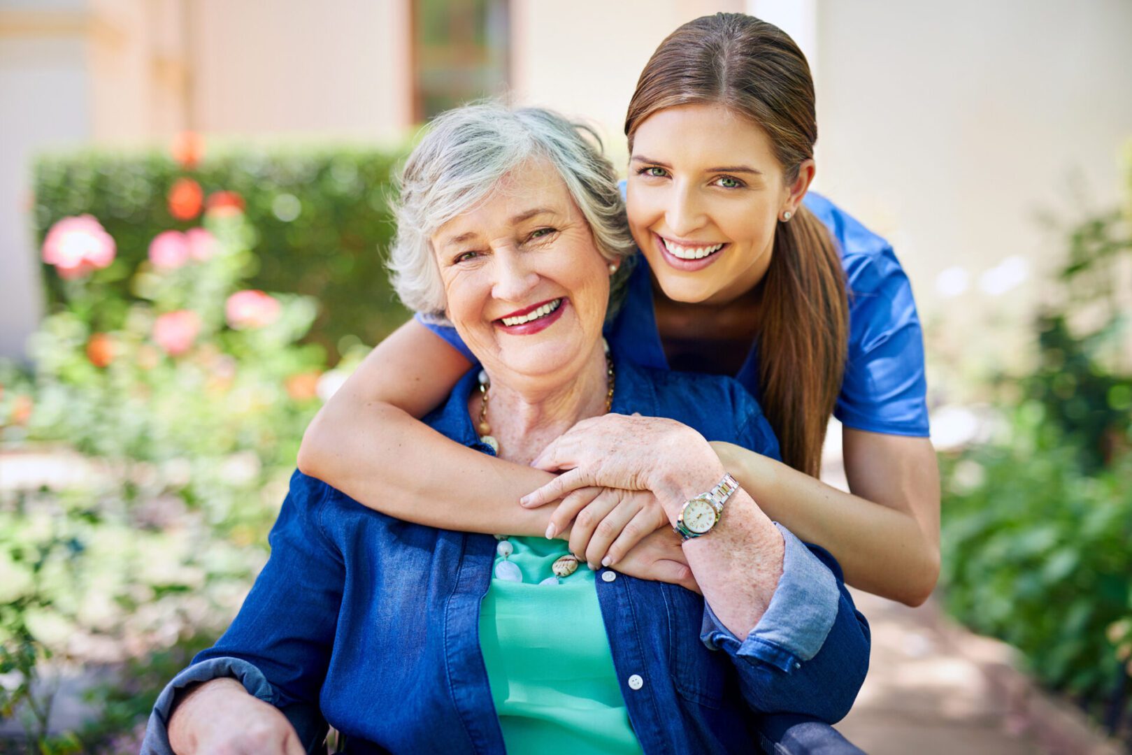 Smiling woman hugging elderly woman outdoors.