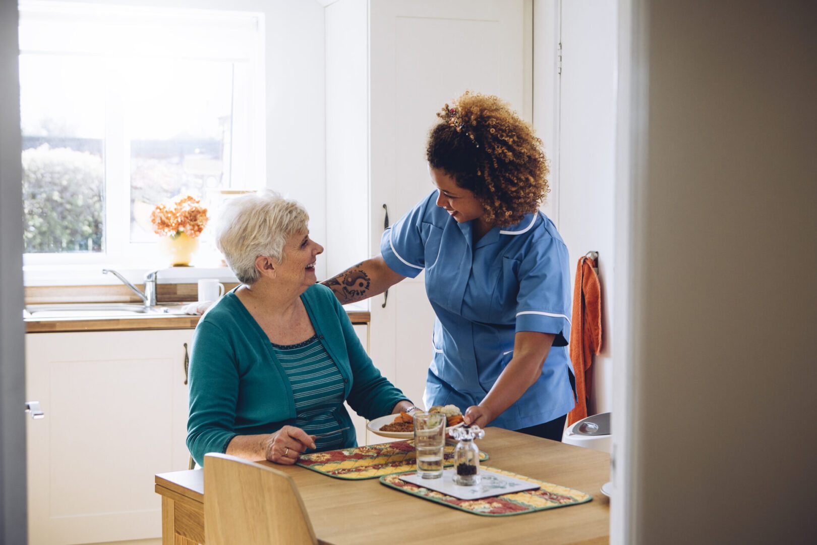 Caregiver assisting elderly woman in kitchen.
